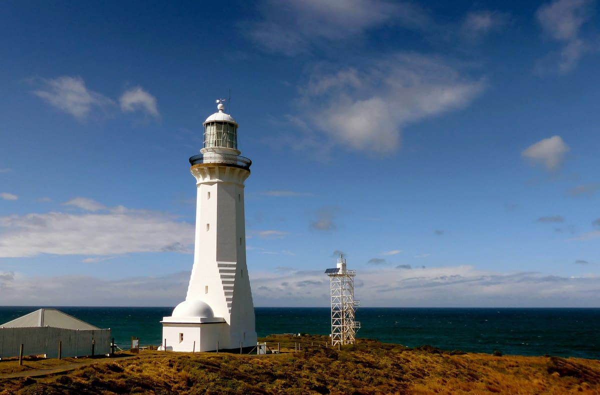 Distant white lighthouse at the tip of a rocky headland, with ocean and sky around it