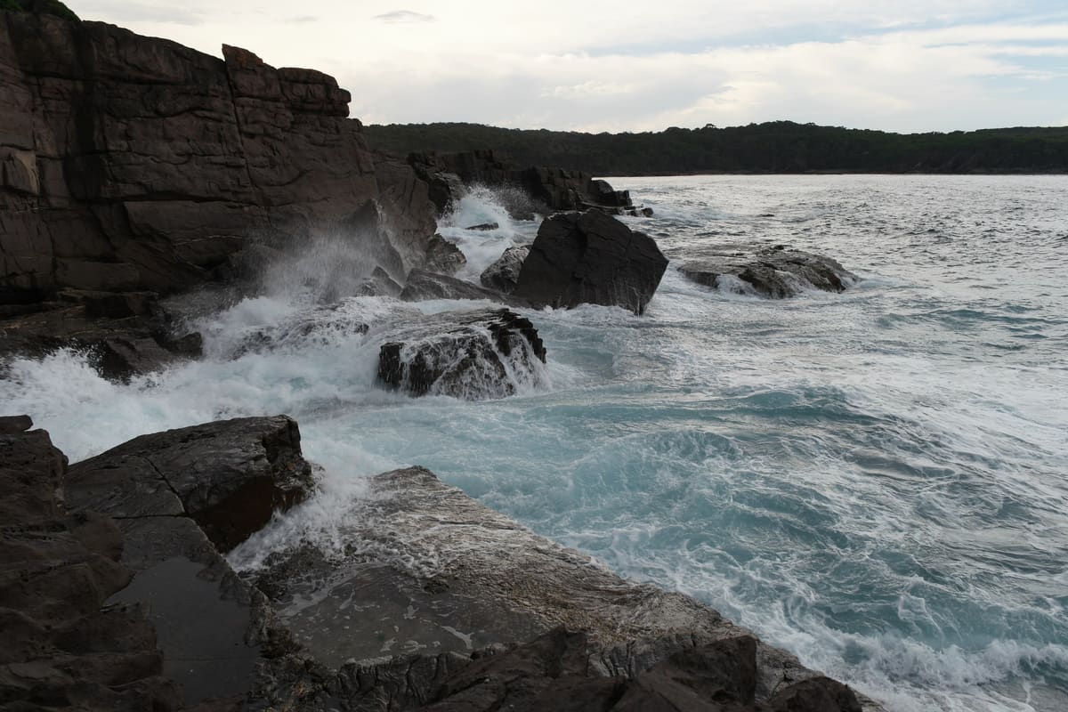 Waves crashing against a dark rocky shoreline with a headland and open sea beyond