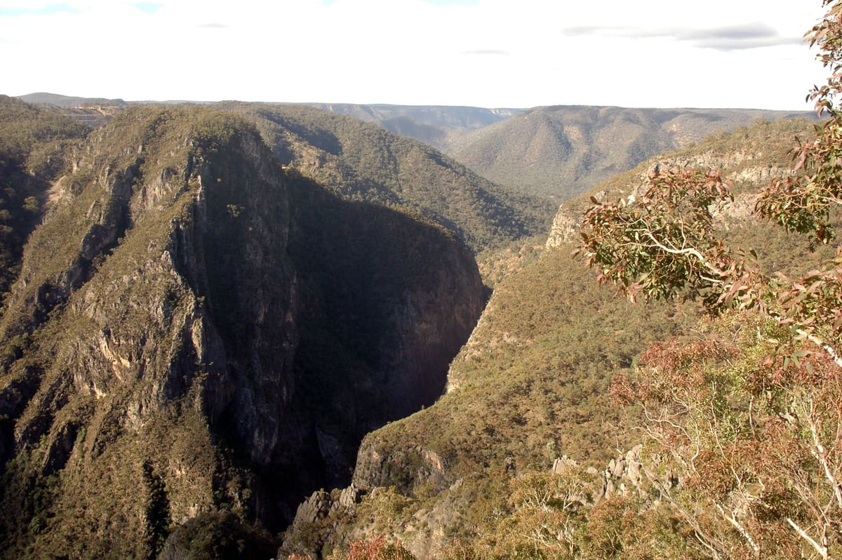 Deep shadowed gorge with a sheer dark cliff face and scrubby ridge under blue sky