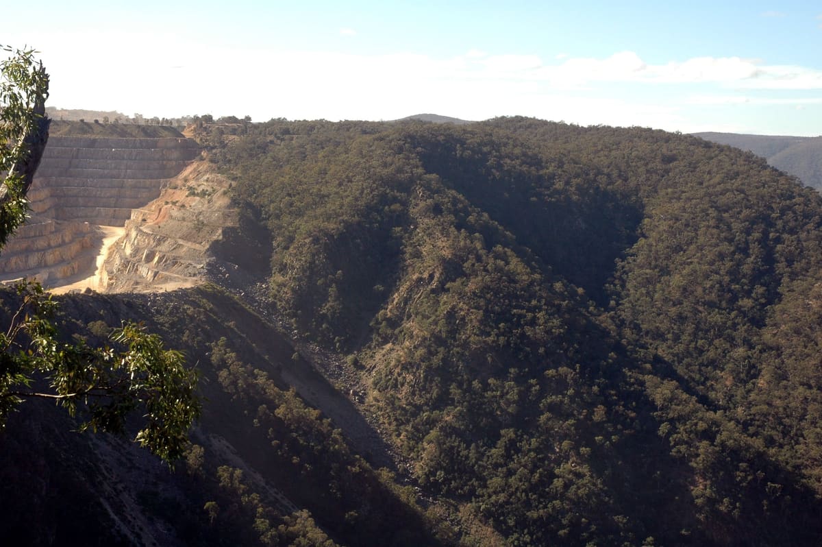 Deep wooded gorge with a pale limestone quarry scar cut into the far hillside