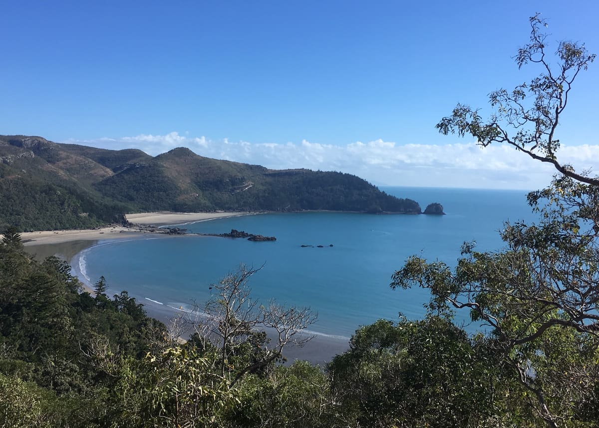 Wide bay panorama of curved beach, headlands and blue sea from a high lookout