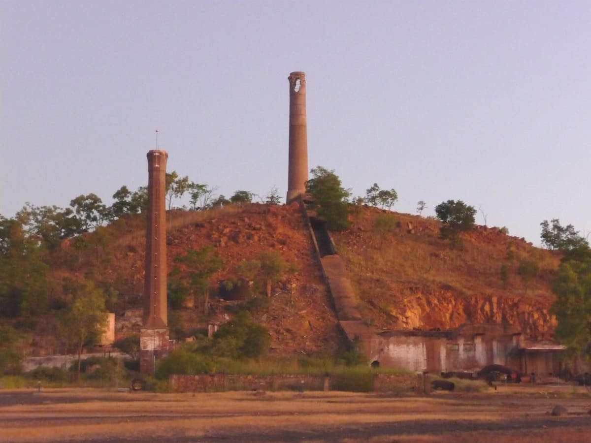 Smelter ruins with two brick chimneys on a red-orange ochre hillside