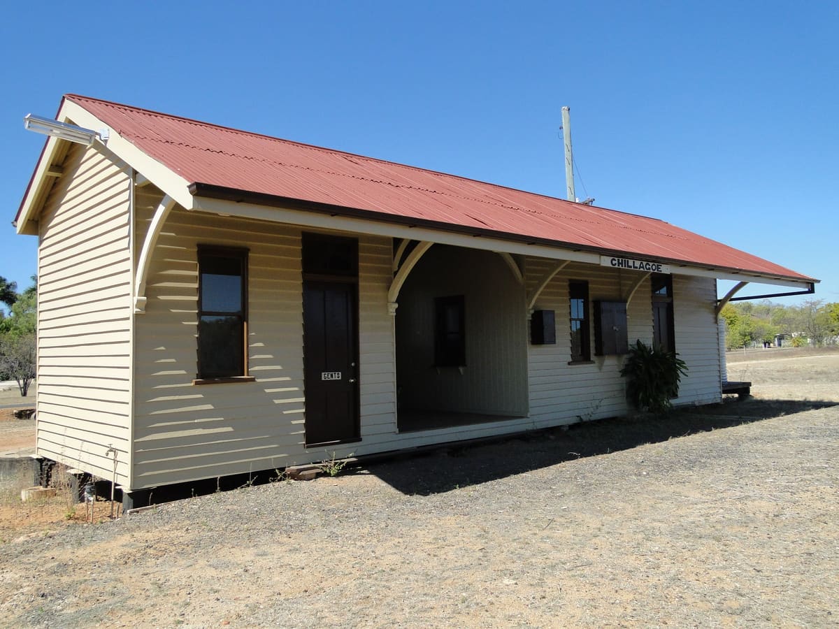 Cream weatherboard station building with verandah and red corrugated roof on a gravel platform