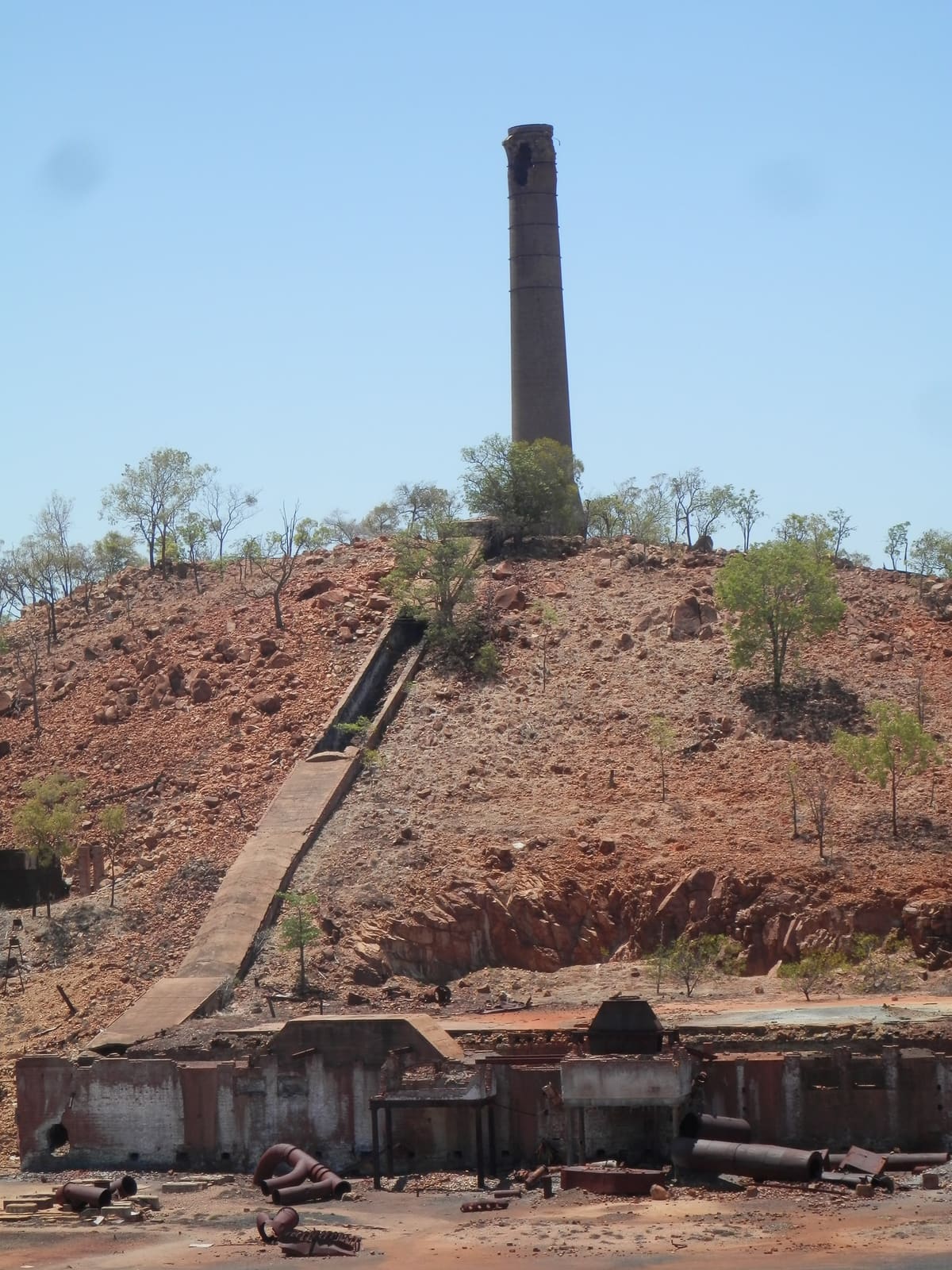Red spoil hill with staircase ramp, chimney at summit, ruined smelter machinery at base