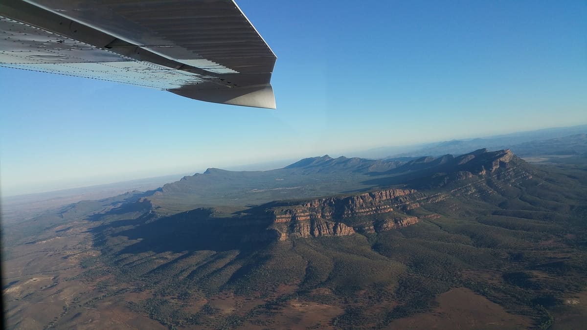 Aerial view of Wilpena Pound, a basin ringed by quartzite walls, seen past an aircraft wing