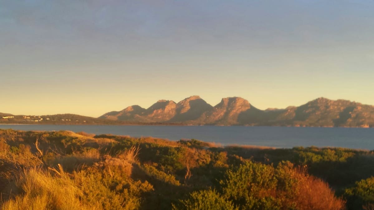 Golden sunset light on The Hazards above calm Great Oyster Bay, with dark scrub in the foreground
