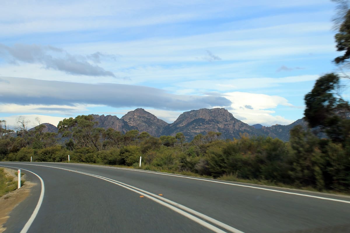 Empty sealed park road curving towards The Hazards mountain range under a cloudy sky