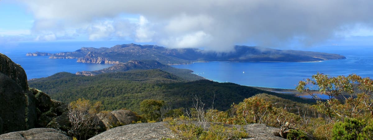 Panorama from Mount Freycinet over forested peninsula and bays to Schouten Island across blue water