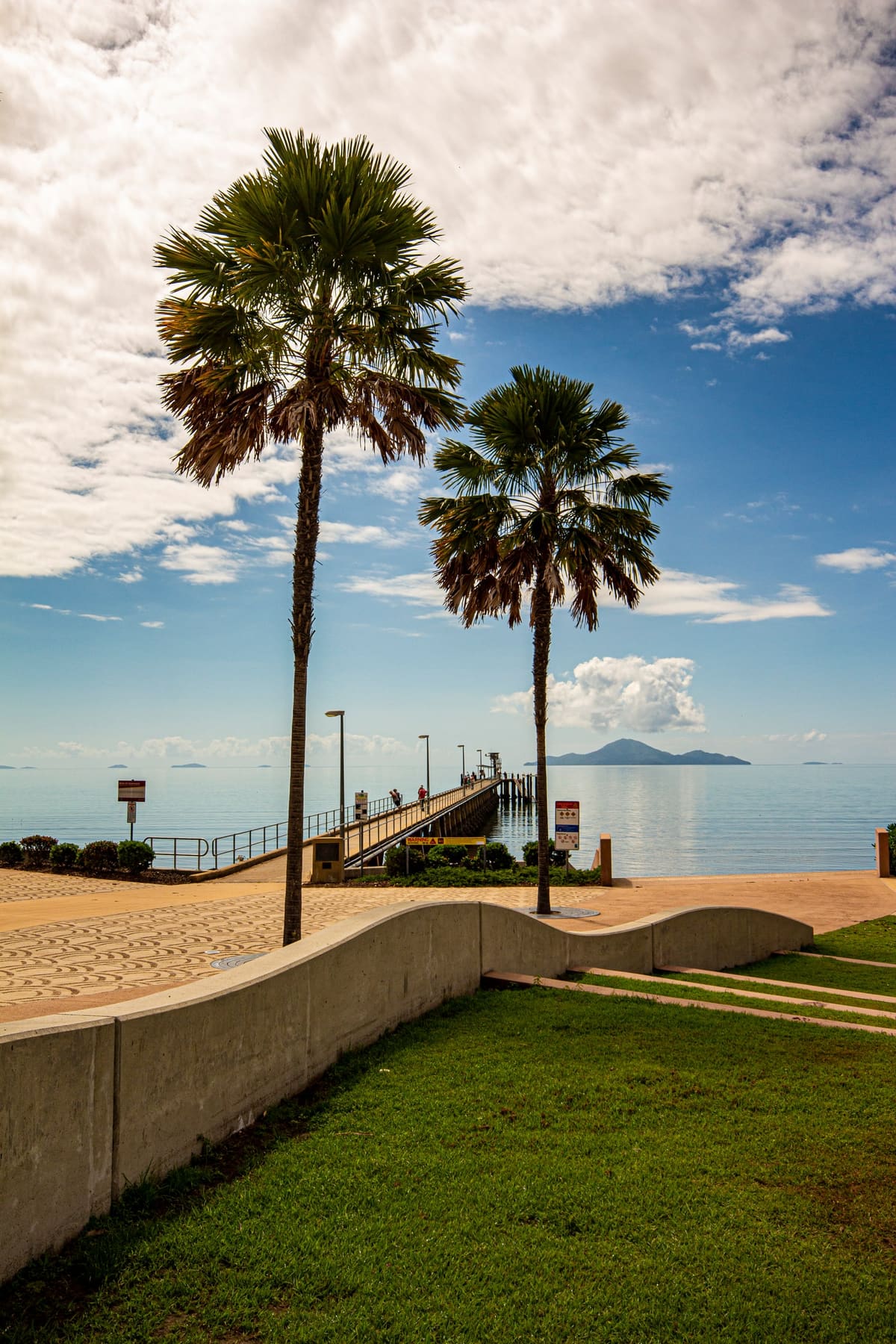 Palm trees along a curved foreshore wall, blue sea and an island across the bay