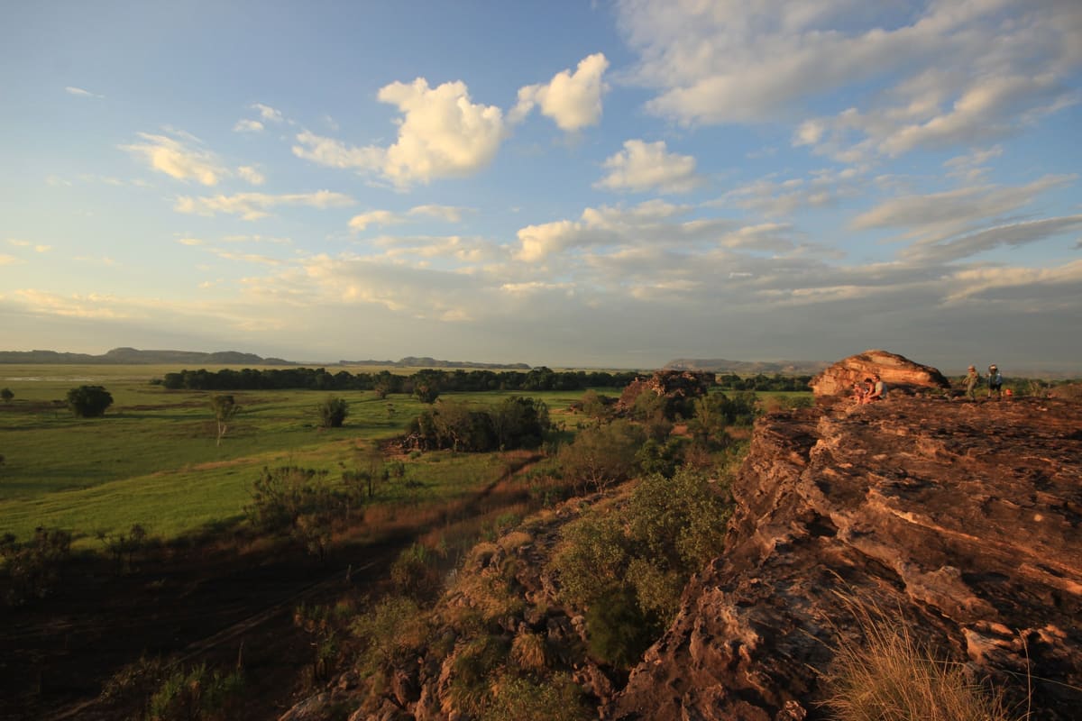 Sweeping view over green floodplain from a rocky plateau under a big sky with fluffy clouds