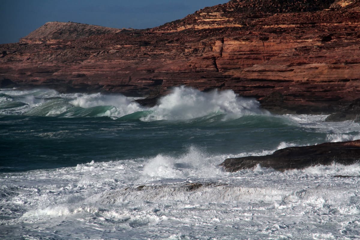 Ocean waves crashing against the stark red layered cliffs at Eagle Gorge