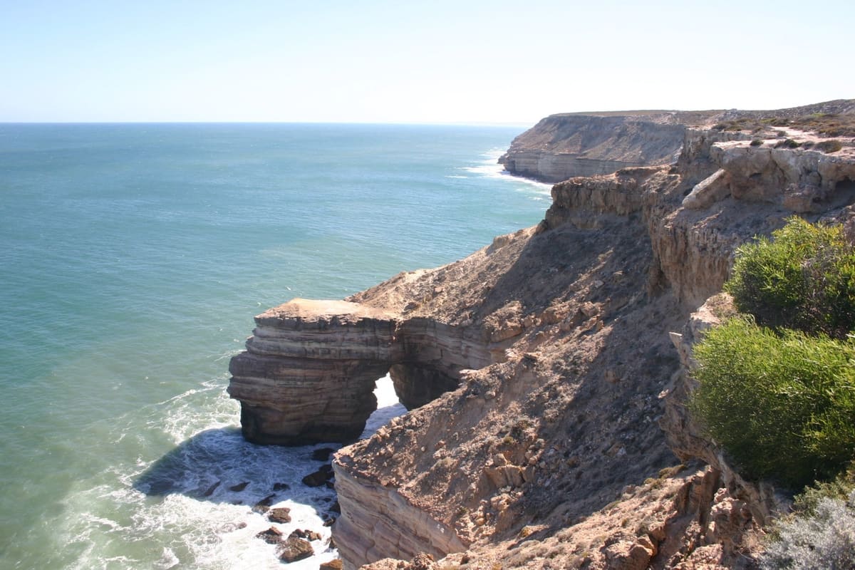 The Natural Bridge rock arch in turquoise surf seen from the cliff above, headland beyond
