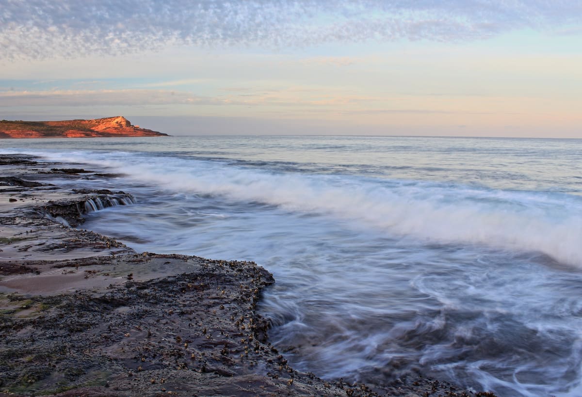 Long-exposure surf washing over a dark rock platform below the Red Bluff headland at sunset