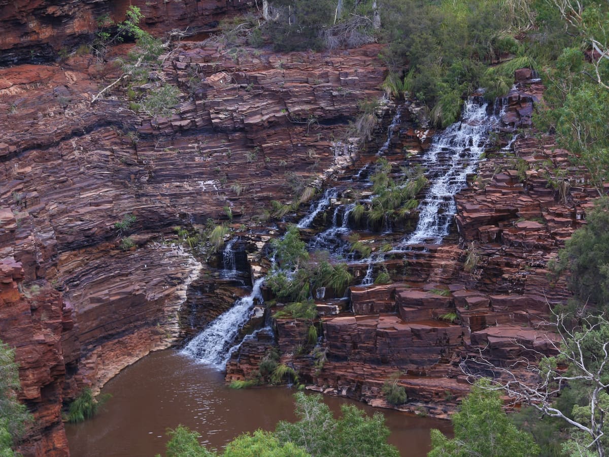 Fortescue Falls cascading down stepped banded rock into a pool, seen from the stairway above