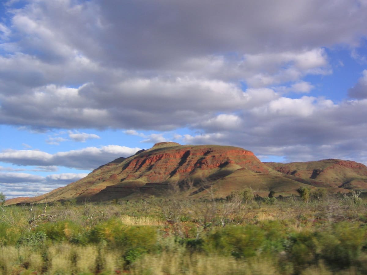 A rounded rocky hill on grassy plains under dramatic clouds in Karijini National Park