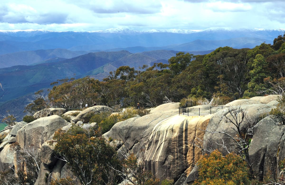 Smooth granite slab with low fence posts, trees and distant blue alpine ranges