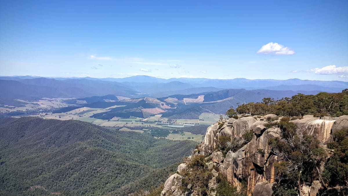 Wide panorama from a granite outcrop over forested ranges and distant farmland