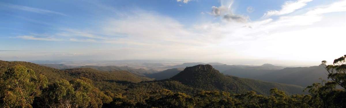 Hazy ridgelines and a flat-topped peak in late-afternoon light from an open lookout