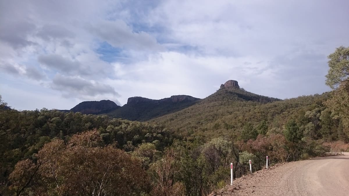Dirt park road curving toward jagged dark peaks under a cloudy sky