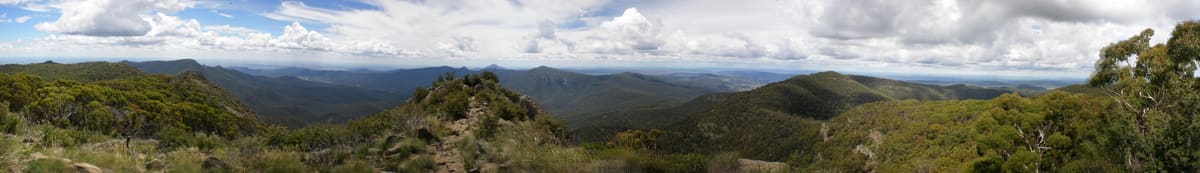 Panorama of forested ridges and far plains under clouds from the summit platform