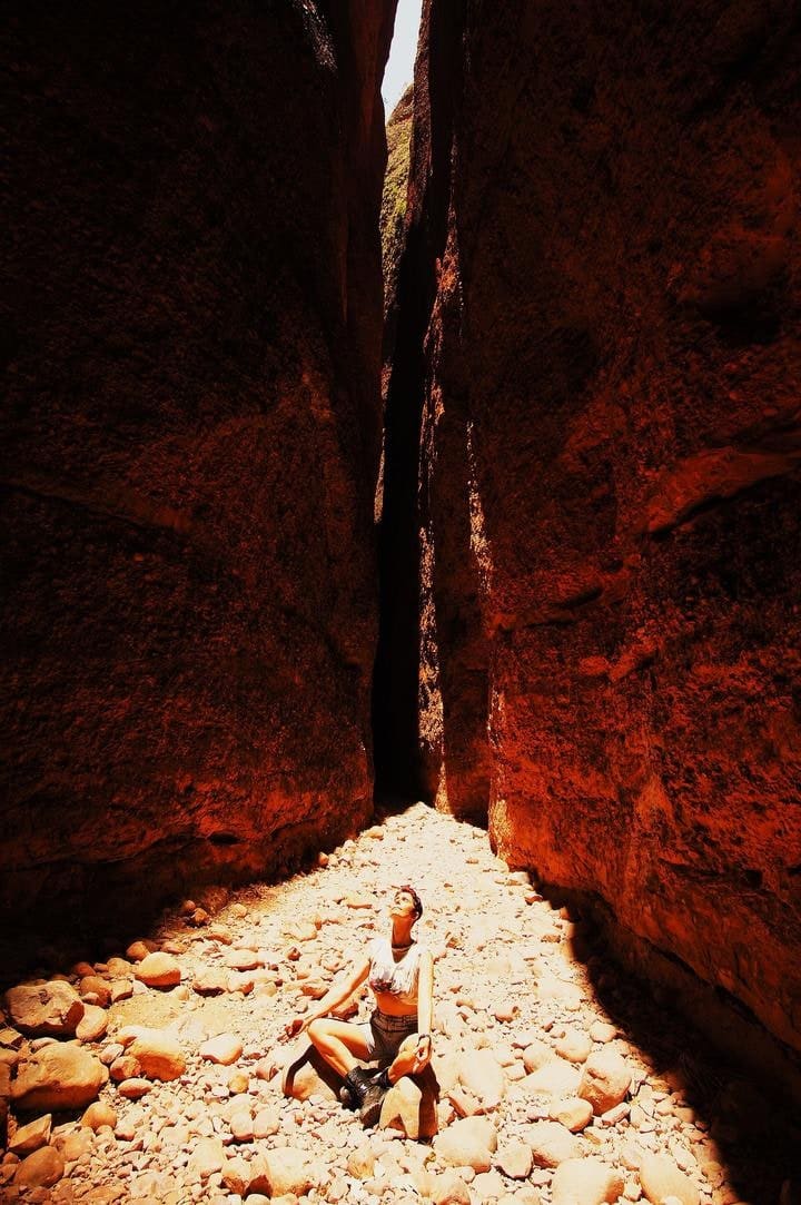 A person walking through the narrow, palm-lined slot of Echidna Chasm in Purnululu National Park, 200m-high walls narrowing to about a metre, shown for scale