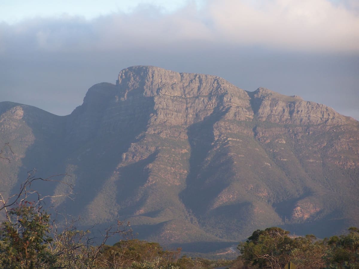 Bluff Knoll's layered rock face in soft, hazy light under low cloud, bushland in the foreground