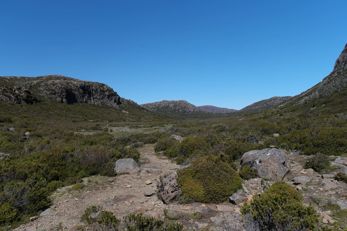 Boulder field and rough walking track through a valley between rocky hills