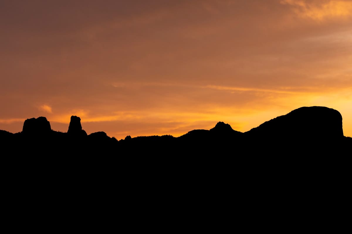 Black silhouettes of volcanic formations against a vivid orange sunset sky