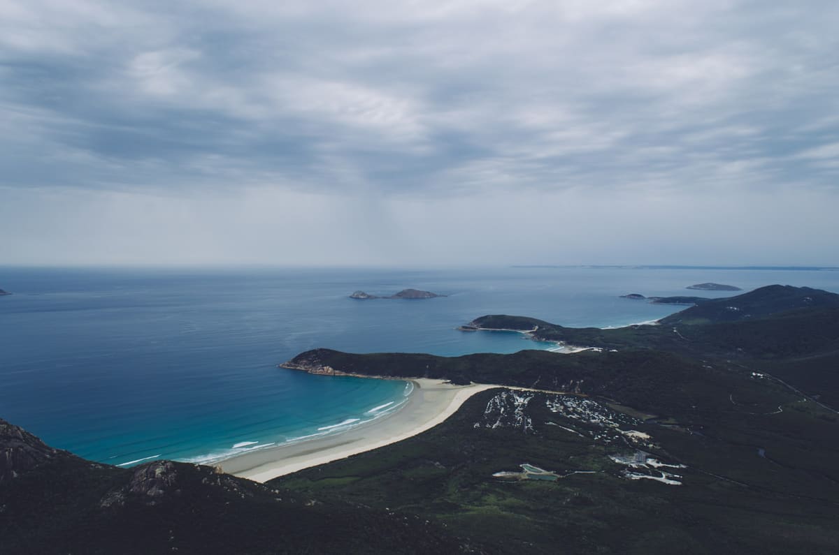 Elevated view from Mount Oberon over turquoise ocean, a white crescent beach and forested headlands with islands offshore