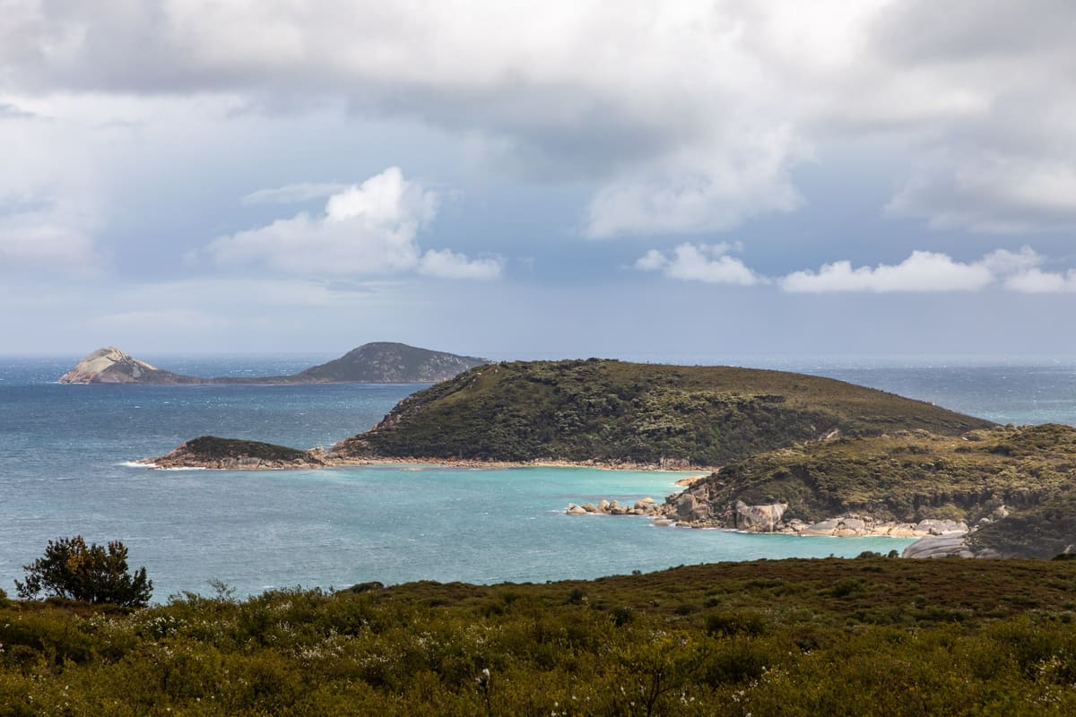 Panorama of Squeaky Beach with turquoise water, granite headlands and islands under a heavy grey overcast sky