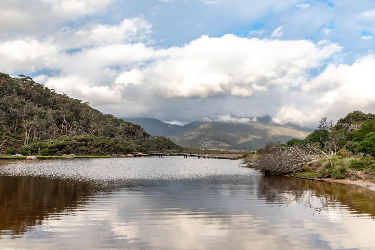 Panorama of the Tidal River lagoon reflecting mountains beneath towering white cumulus clouds