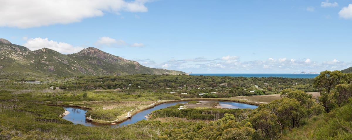 Wide panorama of the Tidal River winding through green flats between ranges and the distant ocean